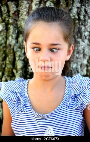 Little Girl fa un volto infastidito dopo aver odorato qualcosa di terribile. I suoi occhi sono incrociati e il suo mento rugosa e i suoi denti sporgono. Foto Stock