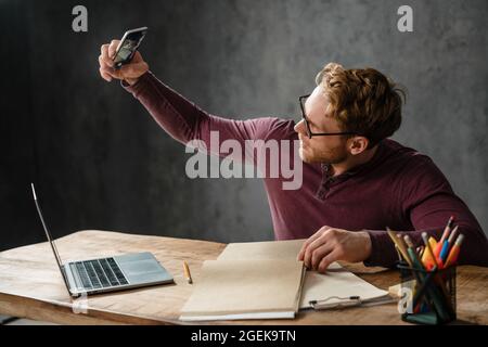 L'uomo seduto al tavolo con carte e computer portatile mentre si fanno foto di documenti in studio Foto Stock