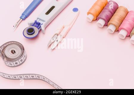 Fondo rosa con accessori per cucire e tessuto. Fili da cucire, aghi, tessuti, nastri da cucire al centimetro o di misura. Spazio di copia. Soppies sartoriali Foto Stock
