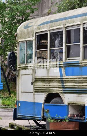 Bus dilapidato e arrugginito con finestre rotte in un'area remota. Foto Stock