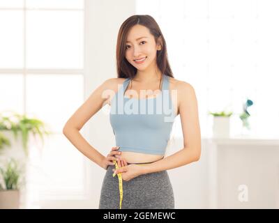 Giovane donna felice che misura la sua vita con un metro a nastro Foto Stock