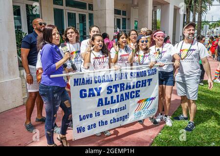 Miami Beach Florida, LGBTQ LGBT Pride Parade partecipanti, gay Straight Alliance studenti ispanici in possesso di banner, donna reporter media reporting Foto Stock