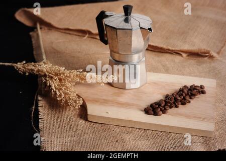 tazza di caffè in alluminio e chicchi di caffè su tagliere in legno su sacco a burlap e sfondo di grano. foto di cibo con concetti minimalisti e vintage per Foto Stock