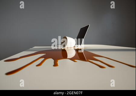 Tazza di caffè nero versato sul computer portatile su un desktop bianco. Foto Stock