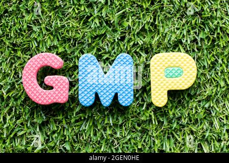Lettera dell'alfabeto del colore in parola GMP (abbreviazione di buona pratica di fabbricazione) su sfondo artificiale verde dell'erba Foto Stock