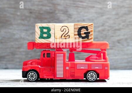 Il camion della scala del fuoco del giocattolo tiene il blocco della lettera in parola B2G (abbreviazione di commercio al governo) su sfondo del legno Foto Stock