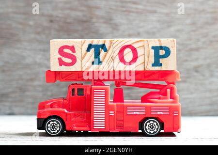 Il camion della scala del fuoco del giocattolo tiene il blocco della lettera in arresto di parola sullo sfondo del legno Foto Stock