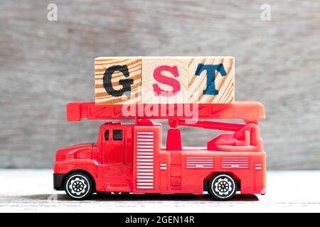 Il camion della scala del fuoco del giocattolo tiene il blocco della lettera in parola GST (abbreviazione dell'imposta di servizi e di merci) su sfondo del legno Foto Stock