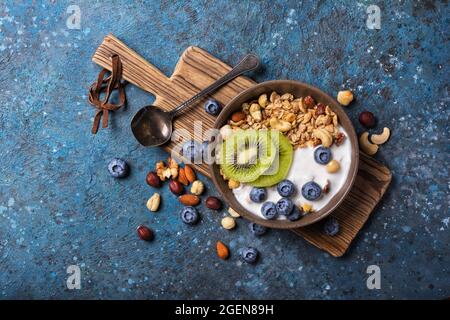 Cibo biologico per una colazione sana e salutare. Vista dall'alto della ciotola con muesli, yogurt, kiwi freschi, mirtillo e noci su fondo di cemento blu Foto Stock
