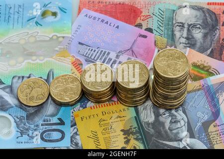 Pile di monete australiane da un dollaro di dimensioni crescenti su varie banconote in dollari australiani. Foto Stock