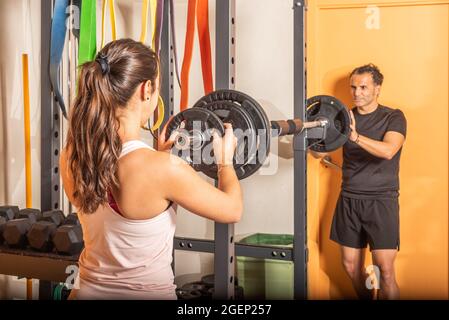 Uomo e donna che mettono il piatto pesi sul bar in palestra Foto Stock