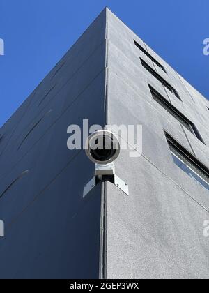 Primo piano di una telecamera di sorveglianza montata sul bordo di un edificio contro un cielo blu Foto Stock