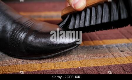 Il primo piano di una spazzola per scarpe sfrega contro uno stivale in pelle nera Foto Stock