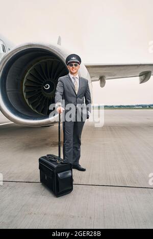 Felice giovane pilota con il suo bagaglio in posa per la macchina fotografica Foto Stock