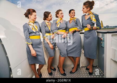 Cinque giovani eleganti e allegre stewardesses che chiacchierano all'aperto Foto Stock