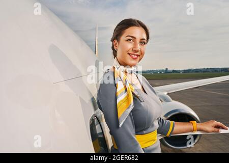 Felice hostess in posa per la macchina fotografica in aereo Foto Stock