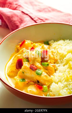 Curry di pollo tailandese con riso in una ciotola rossa e bianca con un tovagliolo rosa Foto Stock