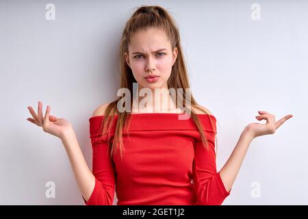 Ritratto di malinteso ragazza dispiaciuto infelice in camicia rossa isolato su sfondo bianco, attraente femmina è perplessa, diffusione Foto Stock