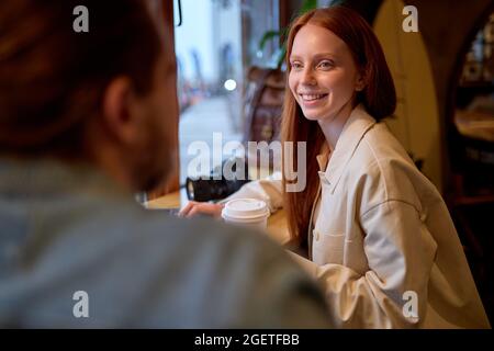 Una donna allegra e un uomo che ride mentre si fa una conversazione positiva in un bar. Due colleghi freelance al tavolo del bar. Concentrarsi sulla redhea Foto Stock