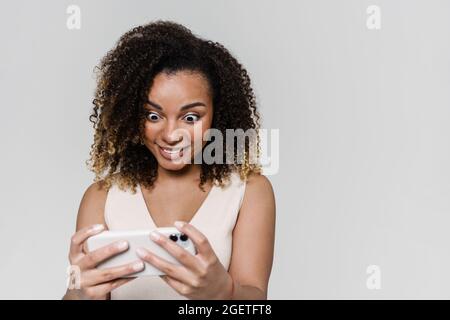 Il ritratto di donna sorpresa guardando il telefono con gli occhi aperti, mentre in piedi in studio grigio Foto Stock