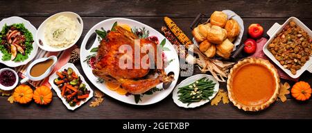 Tradizionale cena di tacchino del Ringraziamento. Vista dall'alto della scena del tavolo su uno sfondo di banner di legno scuro. Tacchino, purè di patate, condimento, torta di zucca e contorno Foto Stock