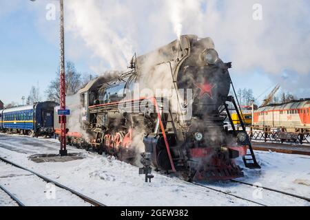 SORTAVALA, RUSSIA - 10 MARZO 2021: Una vecchia locomotiva a vapore sovietica si aggrappa ad un treno passeggeri alla stazione ferroviaria di Sortavala Foto Stock