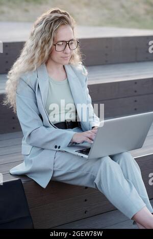 Giovane studentessa seria o donna d'affari che si collega in rete con il laptop in ginocchio Foto Stock