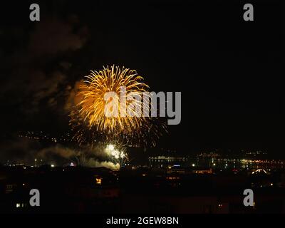 I fuochi d'artificio gialli luminosi lampeggiano con scintille nel cielo notturno scuro su una città sul mare. Giornata della città di Varna con fuochi d'artificio a mezzanotte. Foto Stock