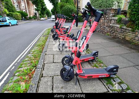 Una fila di voi-e-Scooters visto pronto per la gente a noleggio da cellulare che è fissato al centro del manubrio. Classificato come un veicolo stradale Foto Stock