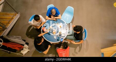 Vista dall'alto di un gruppo di cinque amici maschi che socializzano e bevono al tavolo nella lobby o nel cafe' Foto Stock