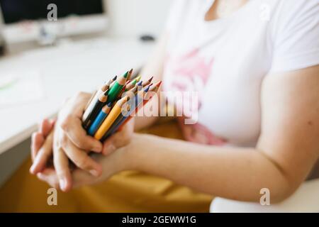 un mazzo di matite colorate nelle mani della donna, computer desk in background Foto Stock