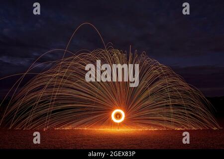 Una ruota di fuoco creata utilizzando lana d'acciaio alight su una ruota di bicicletta di notte per fornire uno sfondo scuro e scintille arancioni Foto Stock