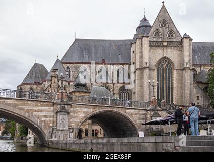 Gent, Fiandre, Belgio - 30 luglio 2021: Sint Michielskerk, churck di San Michele, torri sul ponte e il fiume Leie. Pedoni e ristorante um Foto Stock