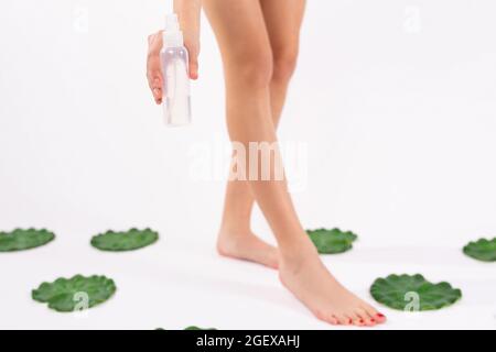 Foto ritagliata di piccole gambe donna con pedicure rosso che tiene in una mano una bottiglia di olio utilizzando dopo l'epilazione alle gambe. Foto Stock