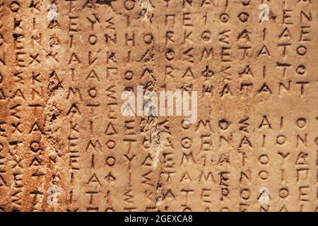 Frammento delle antiche lettere greche usurate scolpite su pietra granata ruvida - archeologia. Foto Stock