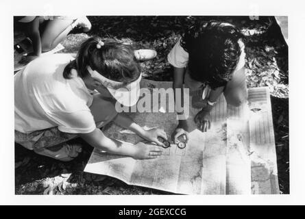 Bandera, Texas USA, circa 1991: Le ragazze di quarto grado usano la bussola e la mappa per stimare la loro posizione durante un viaggio di campeggio di notte della scuola. Originale a colori. ©Bob Daemmrich Foto Stock