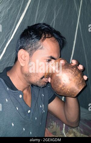 Al mattino, i giovani rurali bevono acqua sui loro letti con una pentola di rame, con zanzariere di fondo Foto Stock