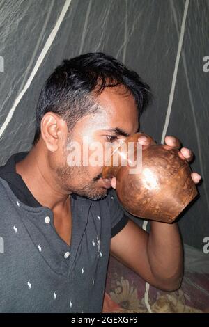 Al mattino, i giovani rurali bevono acqua sui loro letti con una pentola di rame, con zanzariere di fondo Foto Stock