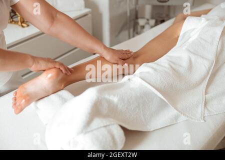 Cliente femminile che riceve un massaggio professionale alle gambe nel salone termale Foto Stock