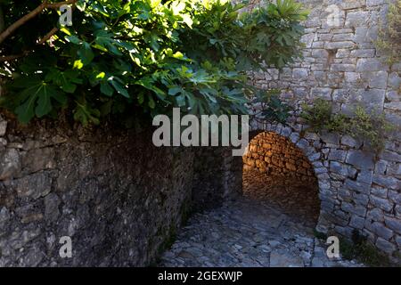 Un passaggio ad arco in pietra, vista sulla strada nel villaggio di Vuno, con la luce del sole che viene dietro l'arco, Albania del Sud Foto Stock