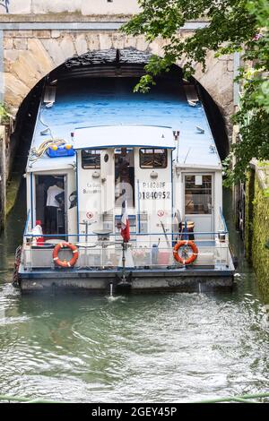 Barca turistica che entra sotto un ponte stretto del canale Saint-Martin a Parigi Foto Stock