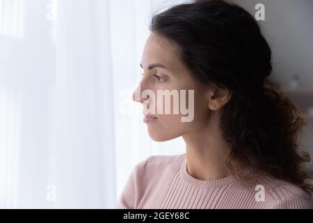 Primo piano faccia di grave ispanica donna guarda fuori la finestra Foto Stock