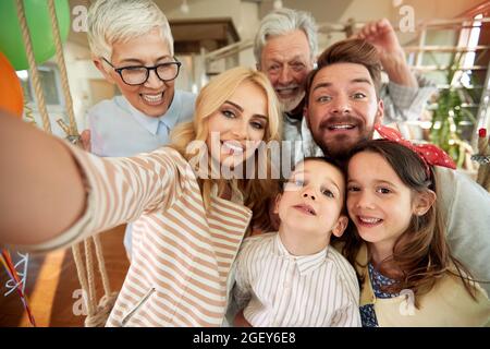 Famiglia di tre generazioni che ha un buon tempo mentre prende un selfie in un'atmosfera allegra a casa insieme. Famiglia, tempo libero, insieme Foto Stock