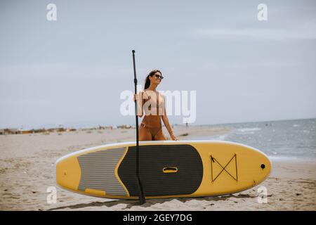 Donne piuttosto giovani con paddle board sulla spiaggia in una giornata estiva Foto Stock