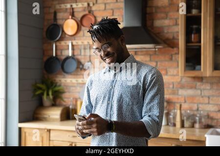 Allegro ragazzo trendy afroamericano che texting su smartphone Foto Stock