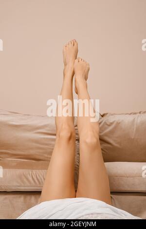 Sottili gambe femminili sul retro del divano (immagine ritagliata) Foto Stock