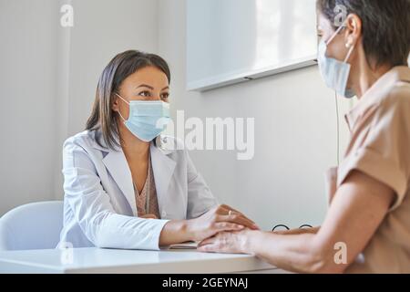 Supporto afro american femmina medico in maschera di tenuta mano di paziente di mezza età Foto Stock