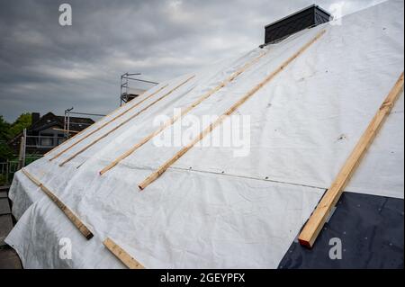 Foglio di plastica sulla parte superiore di una casa privata durante la ricostruzione del tetto. Foto Stock