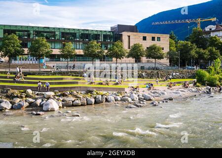 Merano, Alto Adige: Turisti che si rilassano alle bandelle del fiume Passer con le Terme sullo sfondo Foto Stock