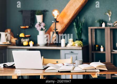 Libro di testo aperto con penna, laptop, pila di libri scoperti che giacciono l'uno sull'altro, tazza di caffè su tavolo di legno in sfondo interno salotto. Online Foto Stock